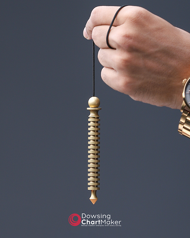Close-up of a hand holding a crystal pendulum over a circular dowsing chart.